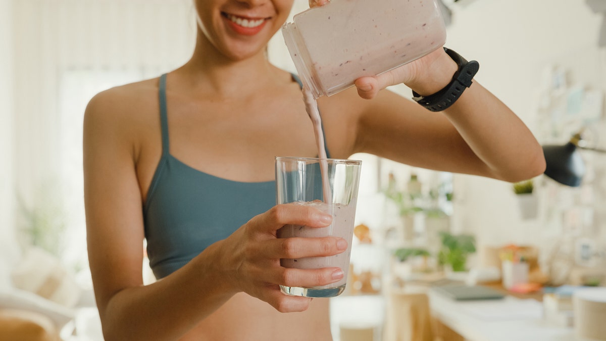 woman using blender and pouring smoothie in glass at home