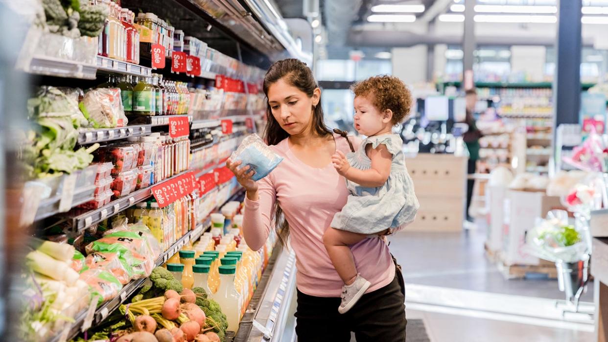 A young mother holds her daughter by the waist while selling groceries