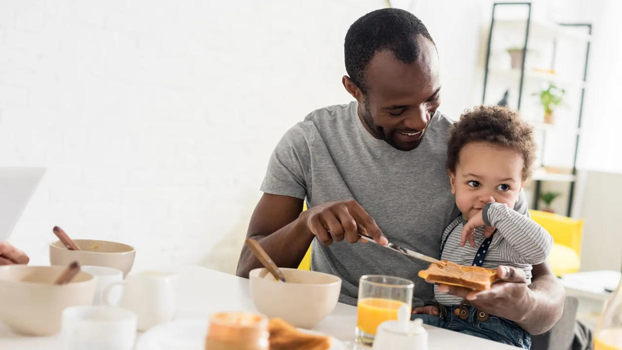 a father spreading peanut butter on toast for a young son