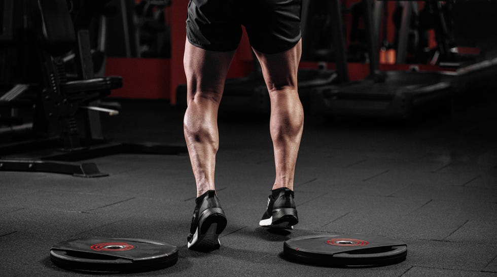 Legs of a trained man with muscular calves in sneakers at the gym